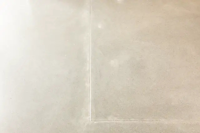 Minimalistisch detail van een naadloze vloer in warm beige met subtiele textuur en perfecte voegen. Het recht perspectief benadrukt de strakke afwerking en serene uitstraling.