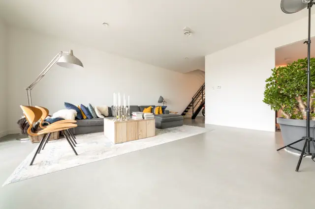 Ruime, lichte woonkamer met naadloze vloer in neutrale tint. De ruimte ademt luxe uit met strakke lijnen, open plattegrond en doordachte styling met moderne meubels en natuurlijke accenten.