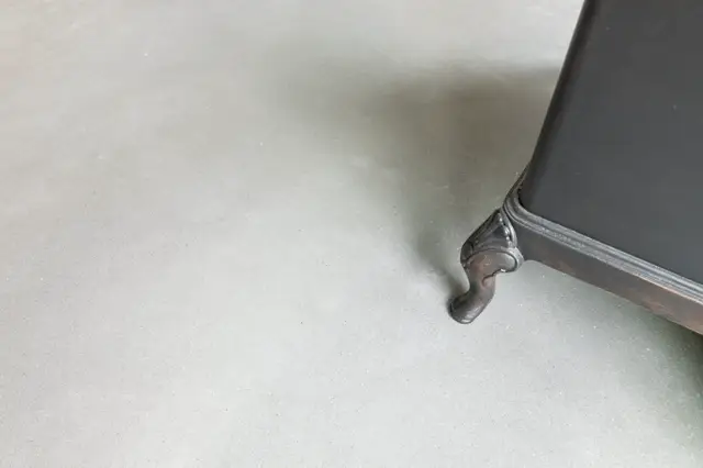 Close-up van een lichte naadloze wand met een elegant metalen wandelement. Het detail toont vakmanschap en de perfecte, fugelloze afwerking van de oppervlakte.
