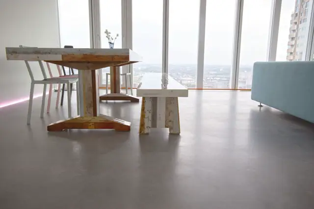 Ruim, licht penthouse met gladde naadloze vloer in warm grijs. Minimalistisch ingericht met industriële meubels en vrijstaande kunstobjecten; panoramische ramen met stadsuitzicht.
