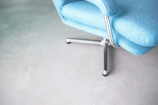 Een strak vormgegeven fauteuil met blauwe bekleding staat op een lichte, naadloze vloer. Het chromen onderstel contrasteert elegant met de rustige ondergrond.