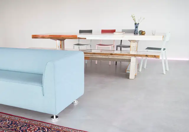 Een licht, rustig interieurontwerp met een naadloze vloer in zacht grijs, minimalistische eettafel en lichtblauwe zitbank. De ruimte ademt rust en elegantie uit met scherpe lijnen en doordachte styling.