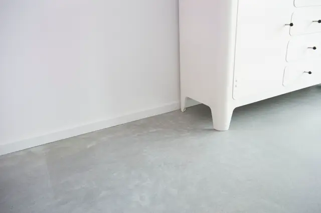 Detailshot van een naadloze vloer in licht grijs met perfect afgewerkte overgang naar witte wand. Schone lijnen, minimalistische inrichting met witte fixtures.