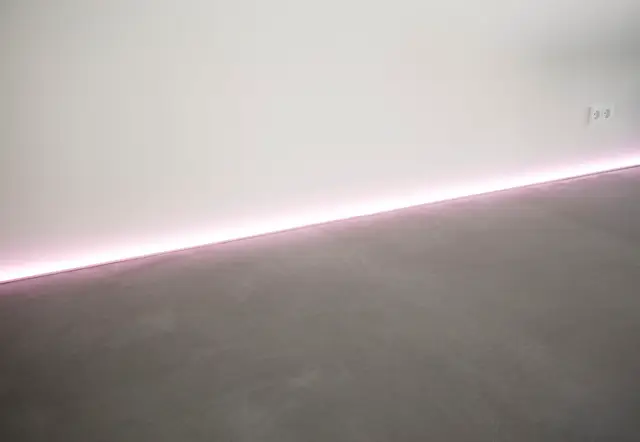 Naadloze wand in licht grijs met subtiele indirecte verlichting in zachtroze. Het vlakke oppervlak benadrukt het strakke, serene design met perfect scherpe lijnen.
