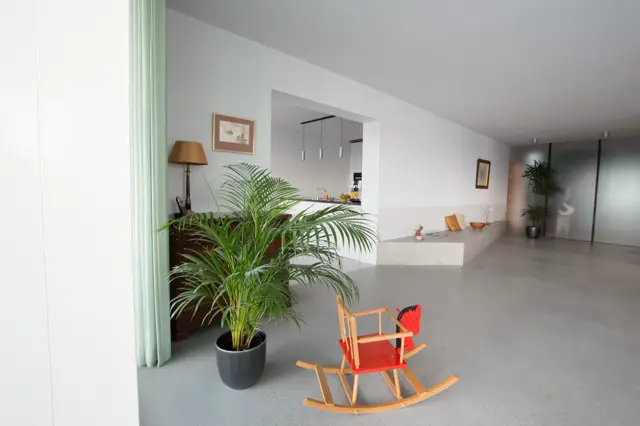 Ruim, minimalistisch interieur met een lichte naadloze vloer die de open ruimte benadrukt. Strak design met witte wanden, groene planten en warme accenten.