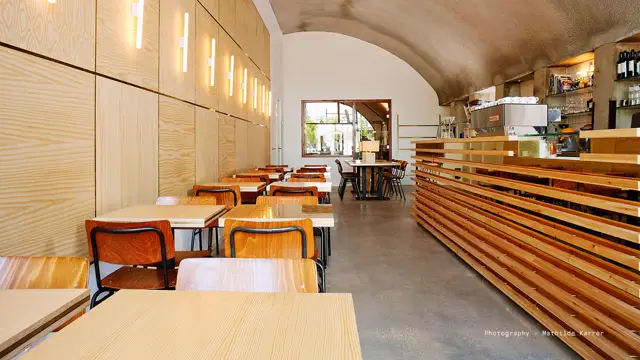 Een sfeervol café met strakke architectuur, warme houttinten en een glanzende naadloze vloer die de ruimte rustig verbindt. Natuurlijk licht stroomt naar binnen via grote ramen.