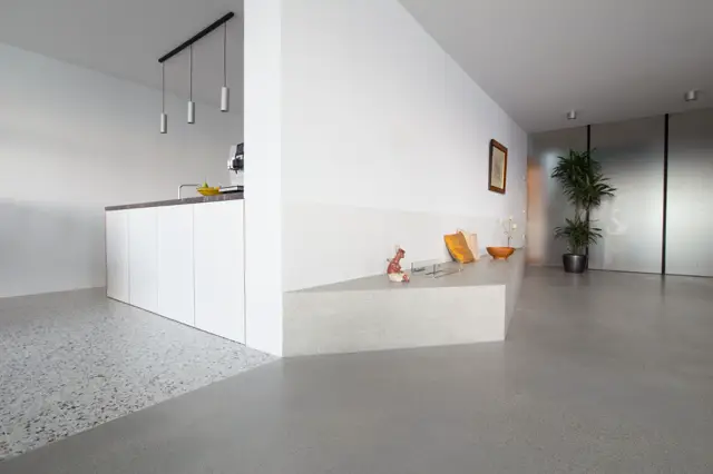Een strakke, lichte openplanconcept met naadloze vloeren in grijs en wit. De ruimte ademt luxe uit door pure geometrie, fijne details en perfect uitgelijnde architectuur.