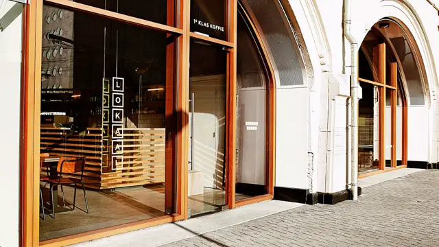 Stijlvolle koffiebar met grote glazen frontale openingen, warme houttinten en een streepdesign. De naadloze vloer loopt soepel door van buiten naar binnen, met scherpe lijnvoering en professionele afwerking.