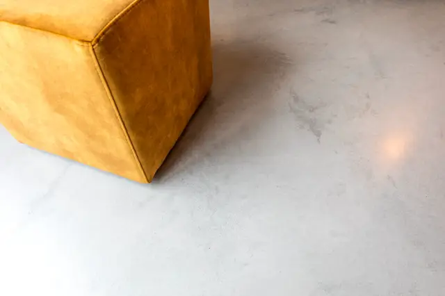 Een modern uitgewerkt minimalistisch interieur met een warm geel leren fauteuil op een naadloze lichte vloer. Het contrast tussen de rijke gouden stof en de rustige, gestructureerde vloer creëert een stijlvol geheel.