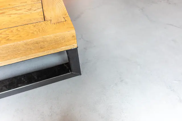 Een heldere afbeelding van een lichte naadloze vloer die elegant aansluit op een houten platform via een strak zwart profiel. Het contrast tussen het minimalistische grijze vlak en de warme houtnerf creëert een modern, opgeruimd esthetiek.