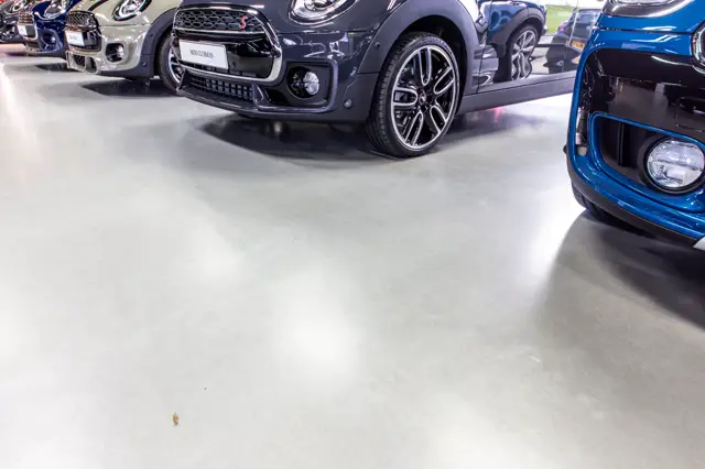 Een schitterende naadloze vloer in een moderne showroom waar exclusieve auto's zijn gepresenteerd. De vloer straalt elegantie uit met zijn lichte, uniforme afwerking en perfect reflecterende oppervlak.