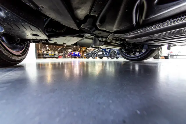 Onderaanzicht van een glanzende, naadloze vloer in een moderne garage met luxe sportauto's. De vloer reflecteert licht en vertoont een strak, schoon afgewerkt oppervlak.