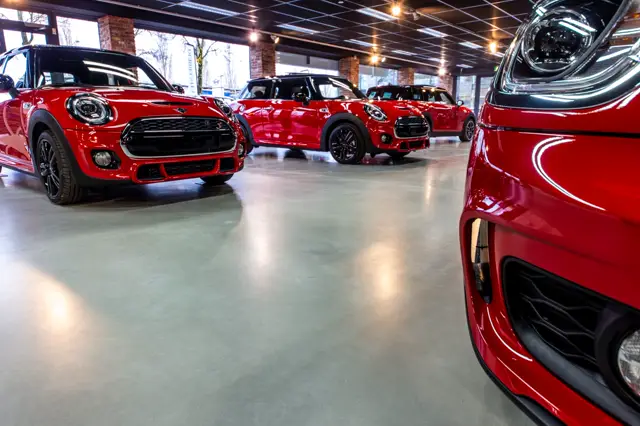 Luxe showroom met glanzende naadloze vloer die perfecte reflecties van auto's en verlichting uitstraalt. De vloer creëert een strak, modern en uitnodigend geheel dat elegantie en kwaliteit uitbeeldt.