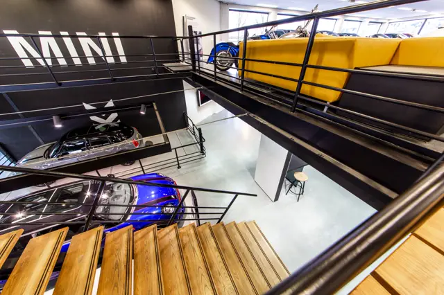 Een strak ingerichte bedrijfsruimte met glanzende naadloze vloer in licht grijs, waarin luxe voertuigen zijn uitgestald. De ruimte ademt minimalisme en precision uit met strakke lijnen, heldere belichting en een galerij-achtige opzet.