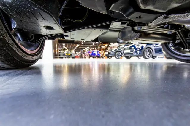 Onderaanzicht van een glanzende, naadloze vloer in een moderne autogarage. De vloer weerspiegelt het licht perfecties en creëert een strak, hightech ambiance rond geparkeerde voertuigen.