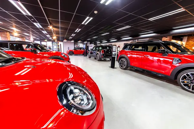 Een moderne showroom met glanzende naadloze vloer, helwit en spiegelglad, waarop exclusieve rode voertuigen zijn tentoongesteld. De ruimte straalt minimalistische elegantie uit met strakke lijnen en professionele verlichting.