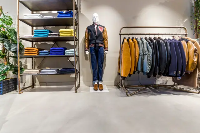 Lichte, naadloze vloer in een modern winkelinterieur met industriële stellingen en kledingrekken. De vloer creëert een schone, uniforme basis die de aandacht op de merchandise richt.