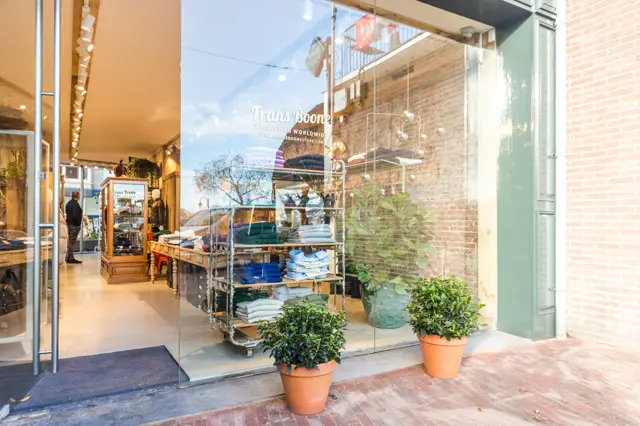 Moderne winkelgevel met naadloze vloer, grote glaspartijen en warme belichting. Ingericht met plantenbakken en minimalistisch merchandising.