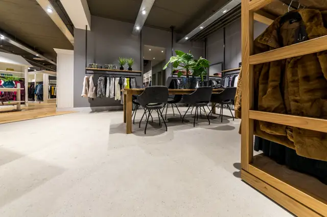 Moderne retail-ruimte met een lichte, naadloze vloer die een strak en minimalistisch interieur ondersteunt. Houtenen display-elementen, donkergrijze wanden en professionele verlichting creëren een exclusieve shopping-ervaring.
