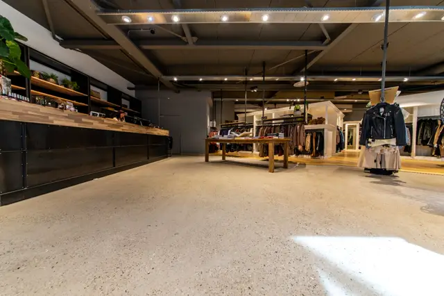 Ruime winkelruimte met heldere naadloze vloer in warme beige tint. Strakke architectuur met geïntegreerde verlichting, houten display-elementen en minimalistisch interieur.