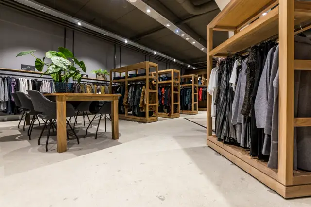 Ruime, licht ingerichte kledingwinkel met een strakke naadloze vloer in warm grijs. De vloer vormt een rustige achtergrond voor houten displaykasten en minimalistische inrichting.