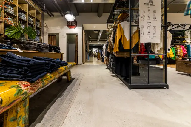 Moderne kledingwinkel met lichte, continue naadloze vloer die het hele interieur verbindt. Strakke opstelling met natuurlijke belichting en schone lijnen.
