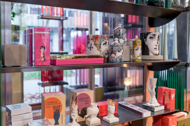 Elegante vitrinepresentatie met kunstobjecten, boeken en decoratieve items tegen een donkere naadloze achtergrond. Schoon, georganiseerd display met strakke lijnen en professionele belichting.