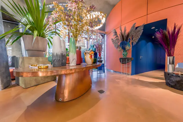 Luxe hal met uniforme naadloze vloer in warm terracottabruin, statige koperen sculptuurobject en geometrische oranje-blauwe wanden met fijne afwerking. Eigentijdse, kuratieve styling met botanische accessoires.