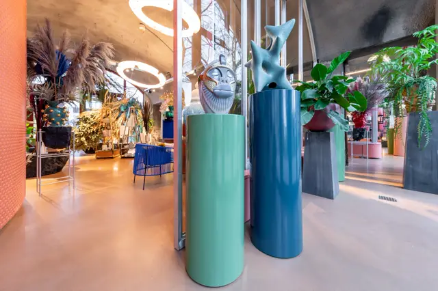 Een moderne bedrijfsruimte met glanzende naadloze vloer in warm beige/zandtint. Strakke architectuur met kleurrijke installaties, groene plantenbakken en minimalistisch design.
