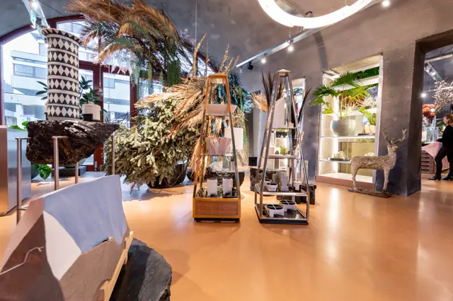 Ruime, lichte showroomruimte met een warme terracotta naadloze vloer. De vloer is volmaakt glad en uniform, omgeven door moderne display-elementen, gedroogde planten en designobjecten die het subtiele kleurpalet versterken.