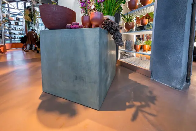 Een ruim, modern interieur met een uniforme naadloze vloer in warm terracotta. Het vlakke oppervlak loopt naadloos door onder naadloze wanden in grijs, met speelse styling van keramische objecten en plantendecoratie.