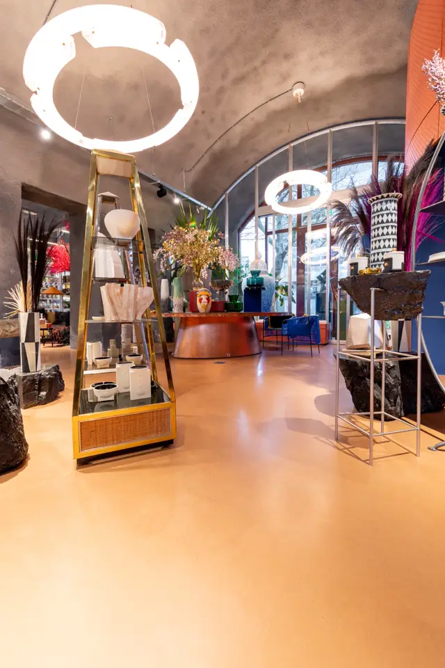 Strak afgewerkte naadloze vloer in warm beige-goud creëert een gepolijste, galerieachtige sfeer in een ruime bedrijfsruimte met architectonische details, moderne verlichting en luxe displays.