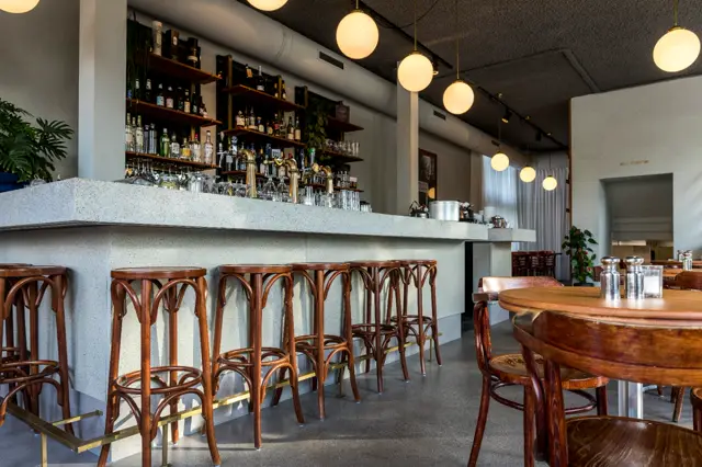 Een stijlvolle barruimte met een schone, minimalistische naadloze wand in licht grijs. Warm houtwerk, elegante hangende verlichting en opgeruimde inrichting creëren een luxe sfeer.