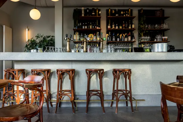 Een stijlvolle bar met lichte naadloze wand, zwarte achtergranden en gouden accenten. Houten barkrukken, geraffineerde sfeer met doordachte verlichting en minimale details.
