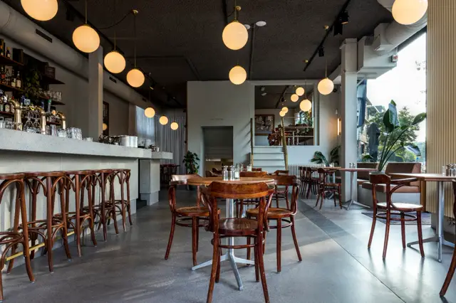 Stijlvolle caféplek met gladdde, grijs-zwarte naadloze vloer die het hele ruimte verbindt. Warme hangende verlichting, houten meubilair en een minimalistisch design creëren een luxe ontspanningssfeer.