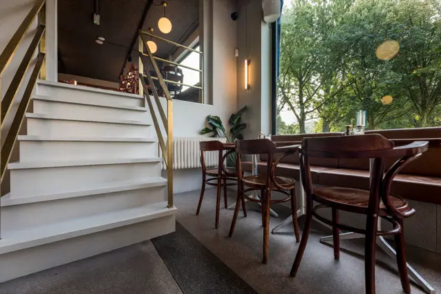 Strakke, naadloze vloer in donkergrijze tint vormt een rustig vloeroppervlak in een elegante hal met witte trap, houten meubels en veel natuurlijk licht van buiten.