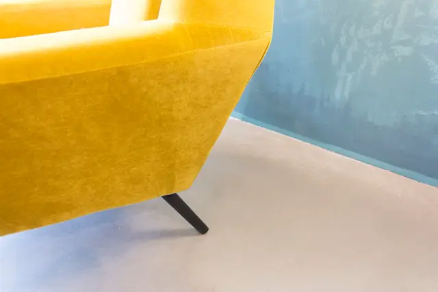 Een stijlvol geel design-meubel staat op een perfecte lichte naadloze vloer, met een blauwe wand op de achtergrond. Het schept een minimalistische, exclusieve sfeer met scherpe lijnen en aangepaste details.