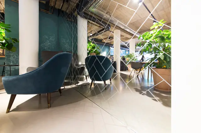 Strakke, lichte naadloze vloer in een ruimtelijk bedrijfsinterieur met designmeubels, groene accenten en natuurlijk licht. De vloer benadrukt de minimalistische, luxe uitstraling van de ruimte.