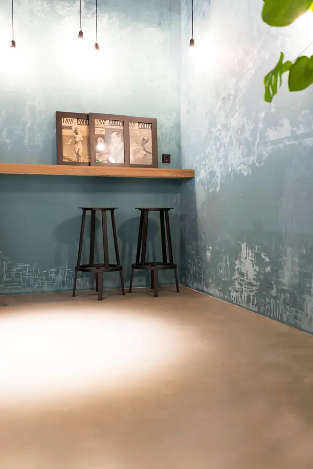 Een serene ruimte met een naadloze wand in gedempte groenblauwtinten, gecombineerd met warme houttonen. Hanglampen en vintage artwork creëren een verfijnd, rustgevend karakter.