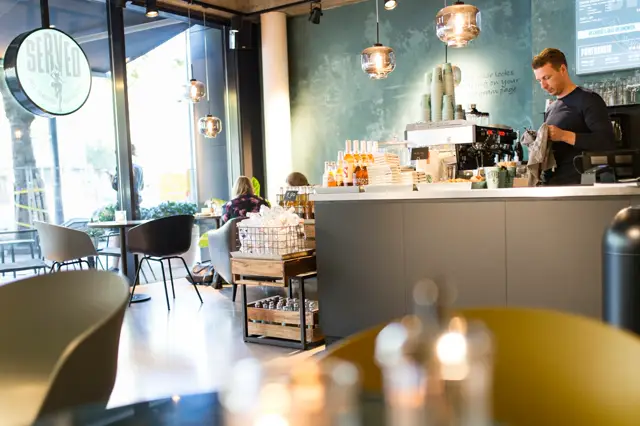 Strak ingerichte koffiebar met glanzende naadloze vloer in grijs. De ruimte ademt rust uit met minimalistisch design, groengeachte wanden en gouden hanglampen.