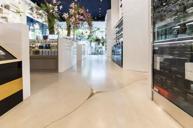 Een strakke, lichte bedrijfsruimte met een naadloze vloer in warm beige. De ruimte ademt elegantie en openheid uit met witte wanden, fijne details in goud en zwart, en een theatrale bloemeninstallatie.