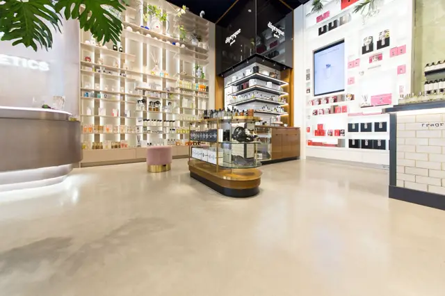 Ruime, moderne beautyretailruimte met een eerlijke, lichte naadloze vloer. De vloer benadrukt de strakke architectuur en minimalistische productpresentatie in een schoon, professioneel interieur.