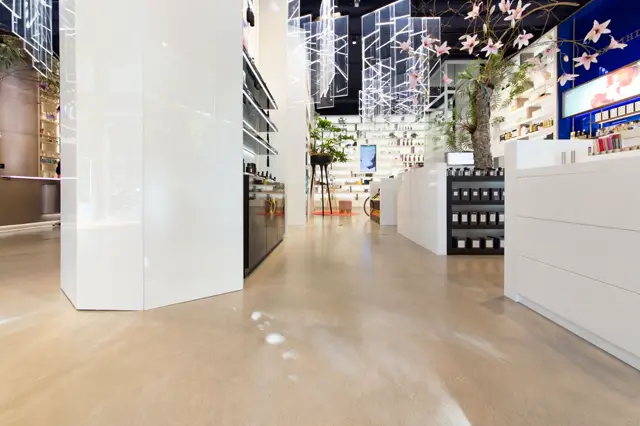 Een strakke, lichte bedrijfsruimte met een glanzende naadloze vloer in warm beige. De ruimte is voorzien van minimalistisch wit meubilair, spotlighting en een verfijnde atmosfeer met decoratieve bloemen.