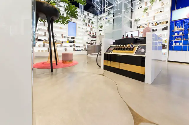 Een moderne beauty boutique met een strakke, naadloze lichte vloer die het hele ruimte visueel verbindt. Minimalistische witte wanden, sculptuuraal zwart-goud interieur en doordachte productuitstalling creëren een exclusieve, gerenoveerde sfeer.