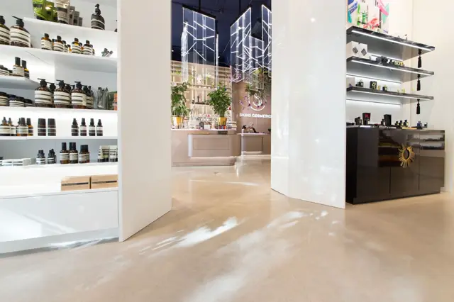 Stijlvolle retailruimte met warme, naadloze vloer en minimalistisch witte wanden. Perfecte staging met verlichte planken, elegante displaykasten en verfijnde winkelinterieur.