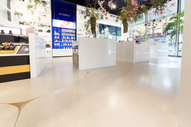 Lichte, minimalistische winkelruimte met glanzende naadloze vloer. Wit meubilair, blauwe accenten en hangende plantengroepen creëren een moderne, opgeruimde sfeer.