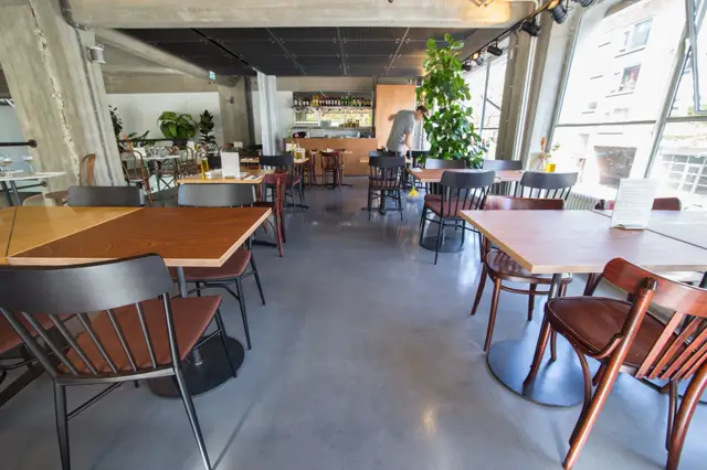 Ruime, lichte restaurantruimte met gladde naadloze vloer in warm grijs. De vloer creëert een schoon, samenhangend oppervlak dat de open, moderne esthetiek ondersteunt.