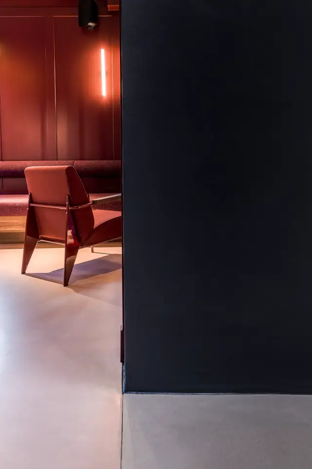 Strak design interieur met contrasterende rode wand en naadloze lichte vloer. Een modern design stoel in rood vormt het centerpiece, verlicht door een minimalistisch neon accent.