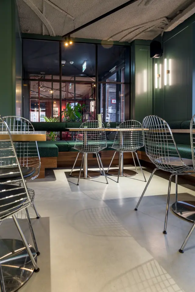 Een elegant verlicht terras met een naadloze lichte vloer die spiegelt in het schijnsel van moderne armaturen. Strakke groene wandafwerking en minimalistisch design creëren een geruststellende, opgeruimde sfeer.