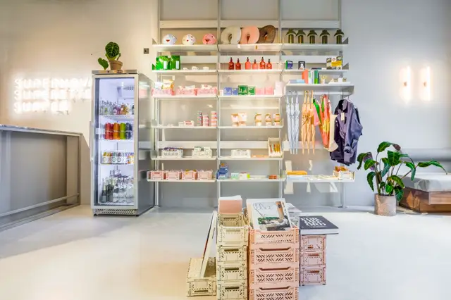 Lichte, moderne winkelruimte met naadloze vloer in warm grijs. Wandkasten met minimalistisch design strak tegen de muur gemonteerd, gevuld met geordende producten en accessoires.